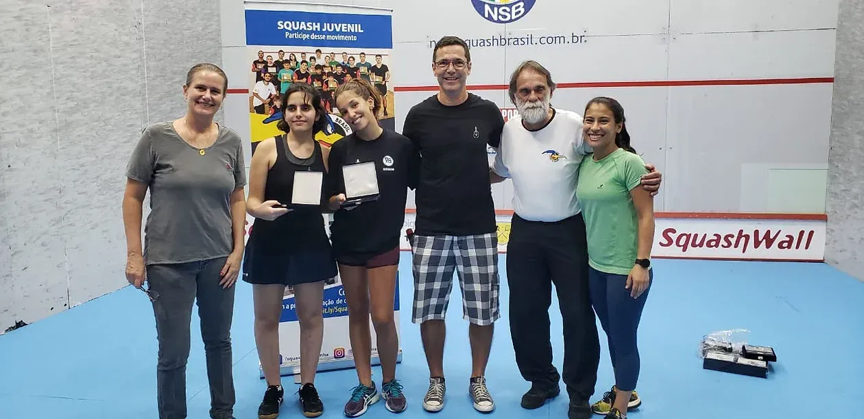 Um grupo de pessoas está posando para uma foto em uma quadra de squash.