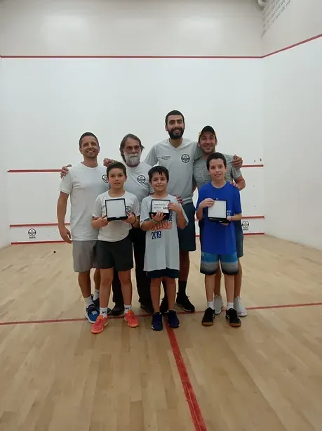 Um grupo de pessoas está posando para uma foto em uma quadra de squash.