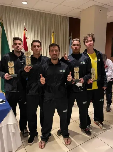 Um grupo de homens de pé um ao lado do outro segurando troféus e fazendo sinal de positivo