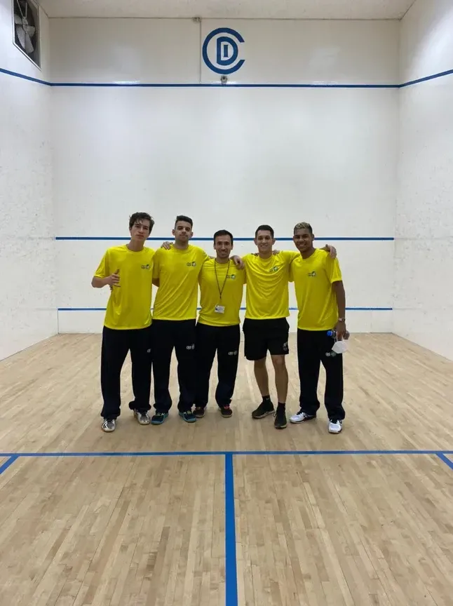 Um grupo de homens está posando para uma foto em uma quadra de squash