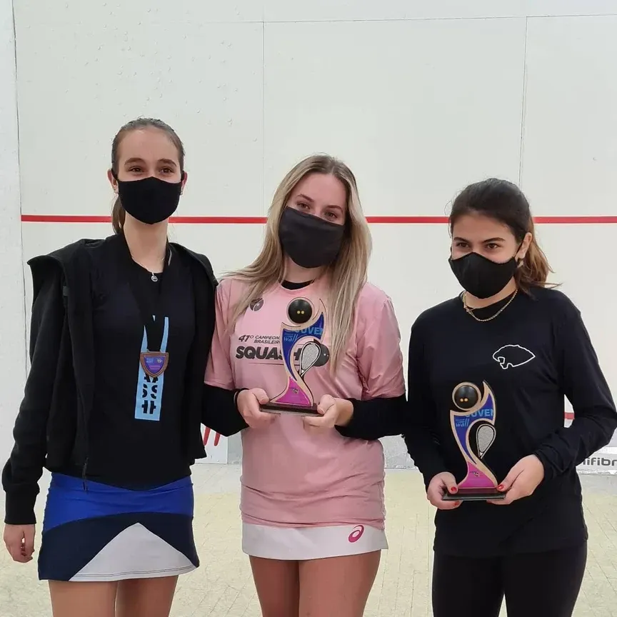 Três mulheres usando máscaras faciais estão segurando troféus