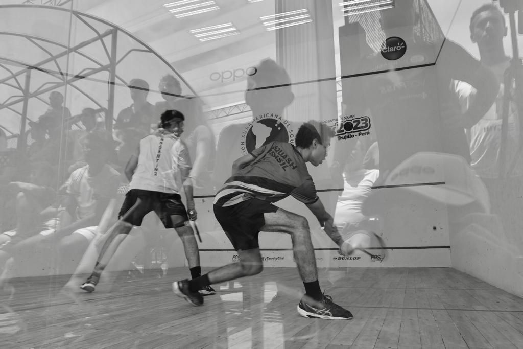 Dois homens estão jogando squash em uma quadra em uma foto em preto e branco.