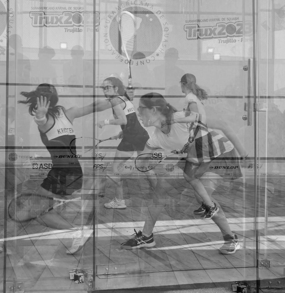 Um grupo de mulheres está jogando squash em uma quadra de vidro.