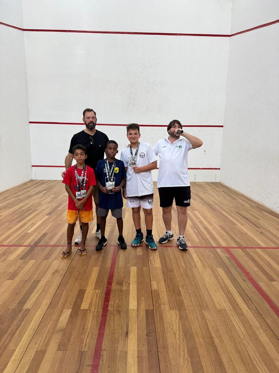 Um grupo de pessoas está posando para uma foto em uma quadra de squash.