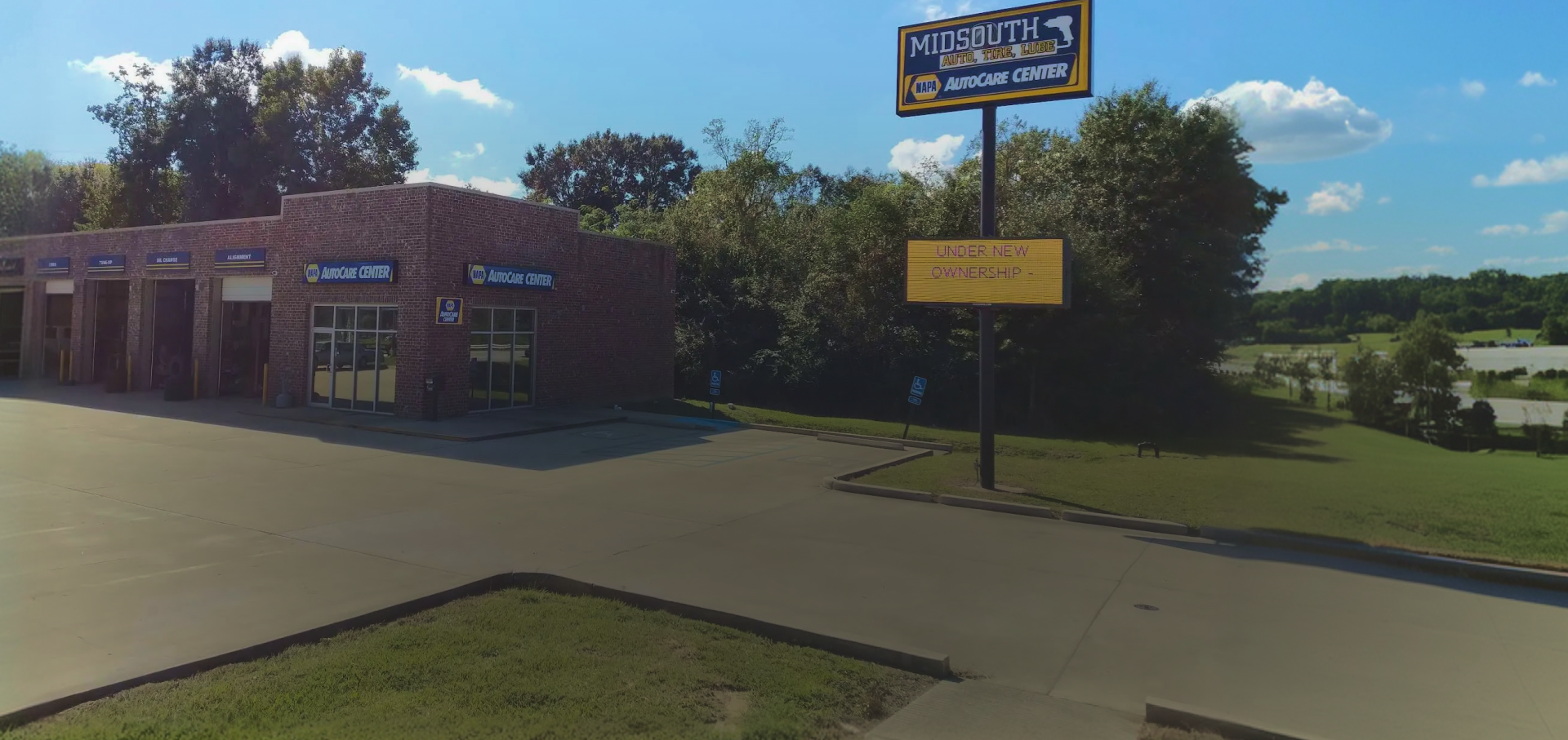 A brown, textured commercial building with service bays next to a tall sign under a clear blue sky on a sunny day.