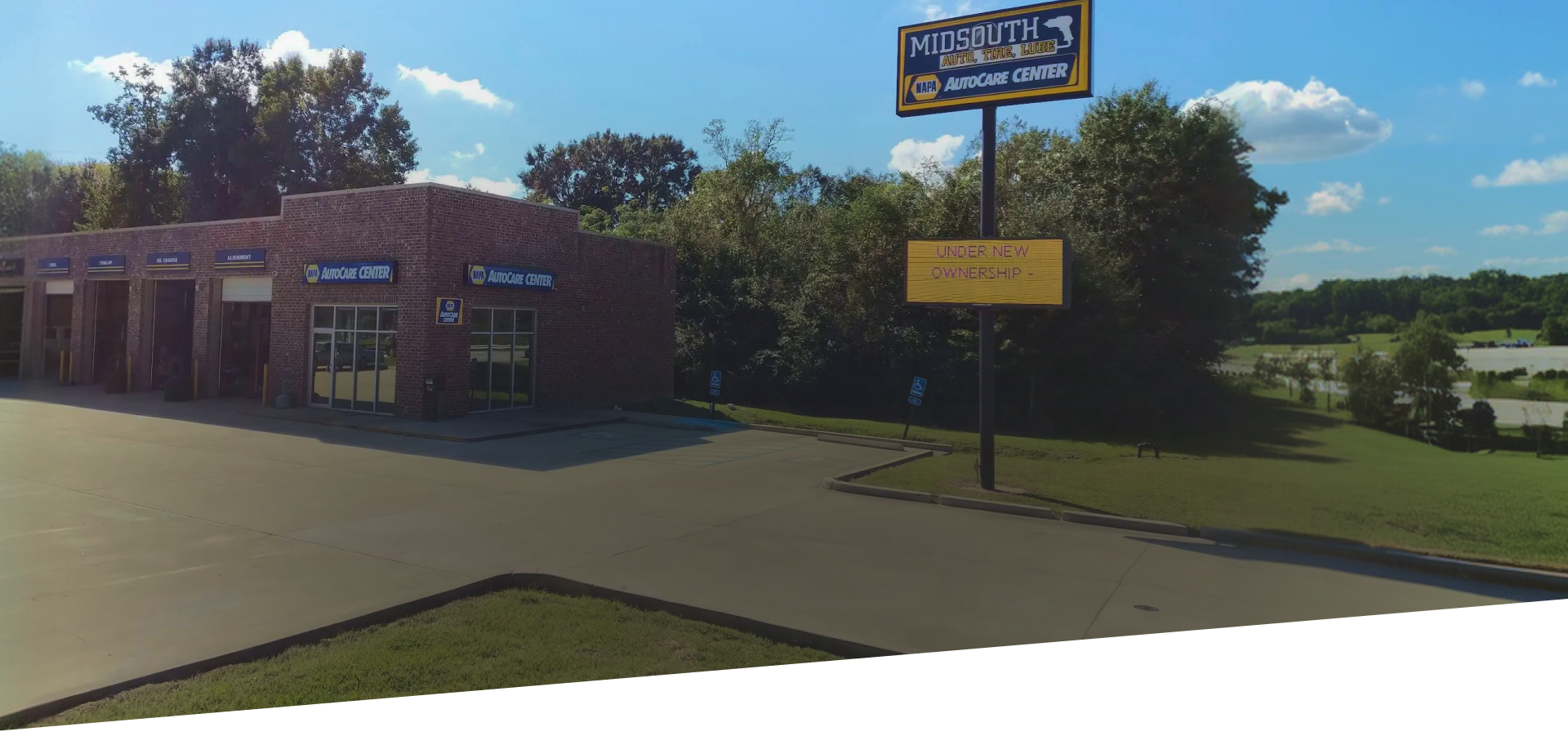 A car wash business with a large sign and a yellow sign on the pole. Blue sky with white clouds.