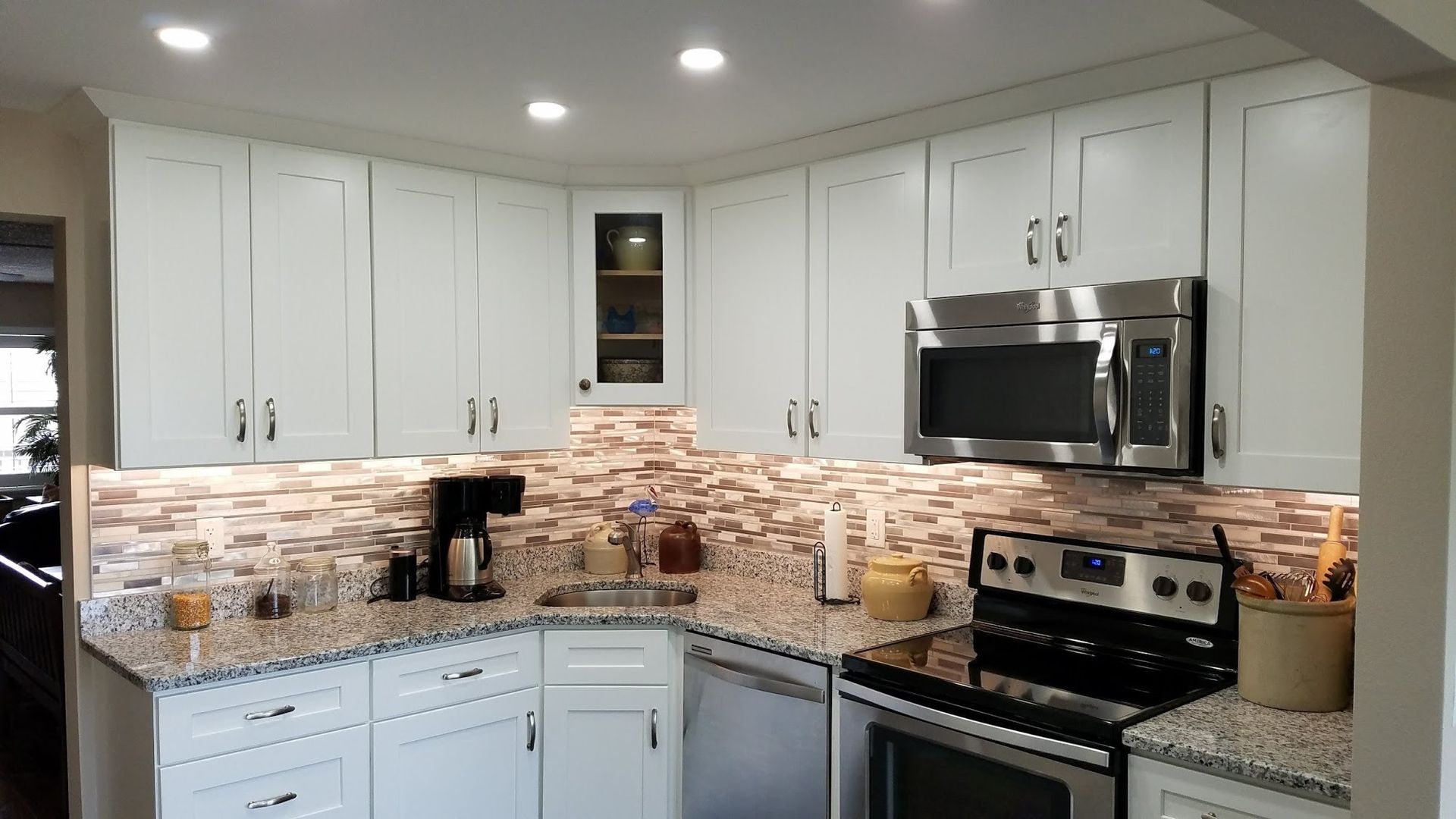A kitchen with white cabinets , granite counter tops , stainless steel appliances and a microwave.