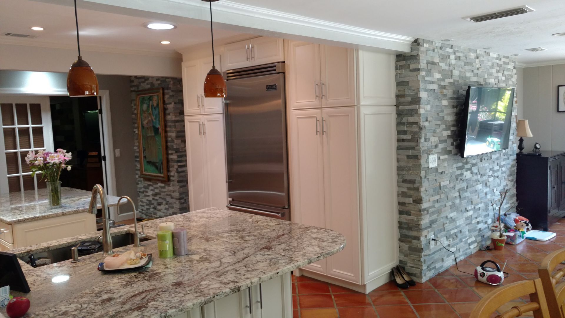 A kitchen with granite counter tops , stainless steel appliances , and a flat screen tv.
