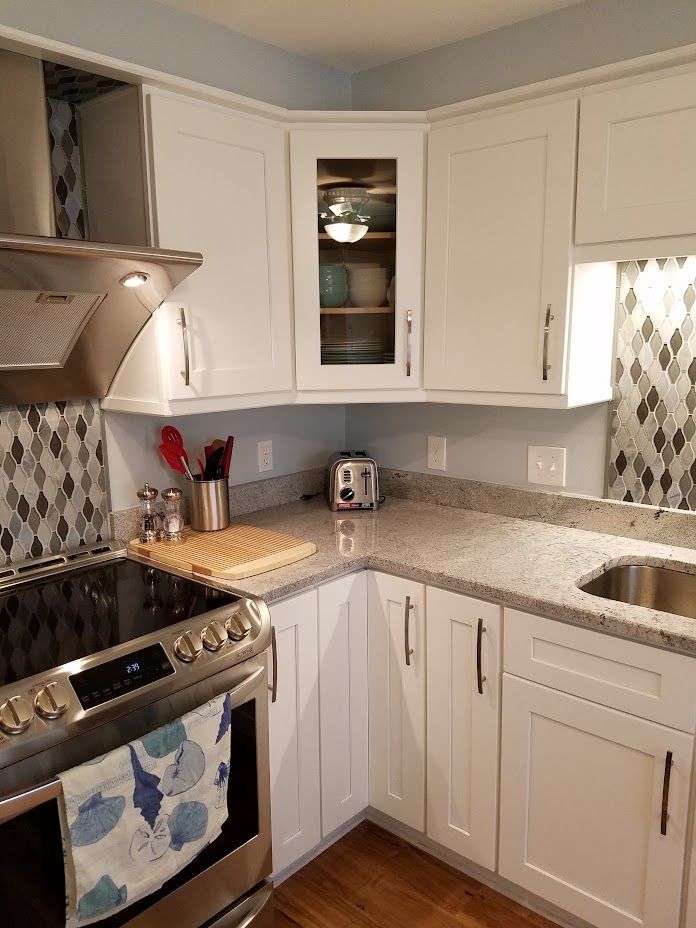 A kitchen with white cabinets , a stove , a sink , and a toaster oven.
