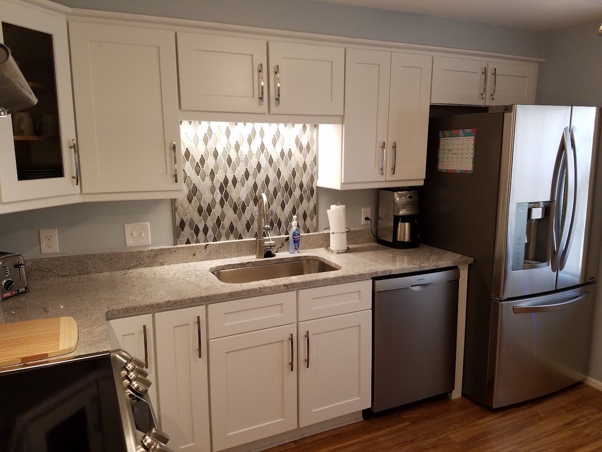 A kitchen with white cabinets , a stainless steel refrigerator , a sink , and a dishwasher.
