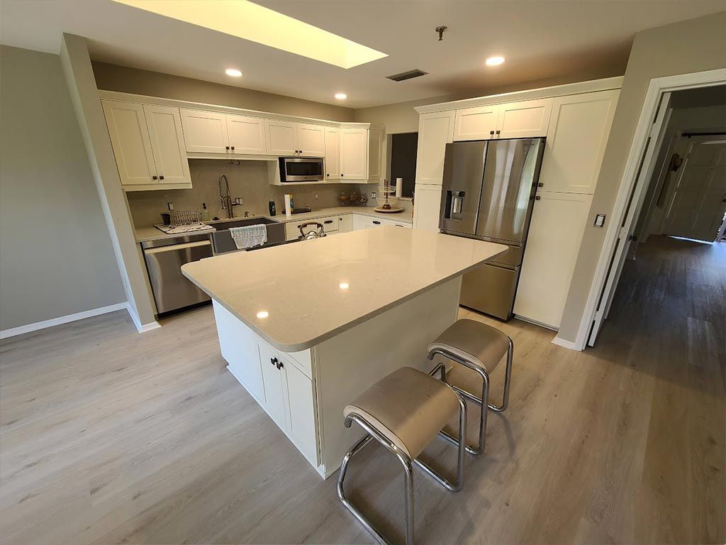 A kitchen with white cabinets , stainless steel appliances , and a large island.
