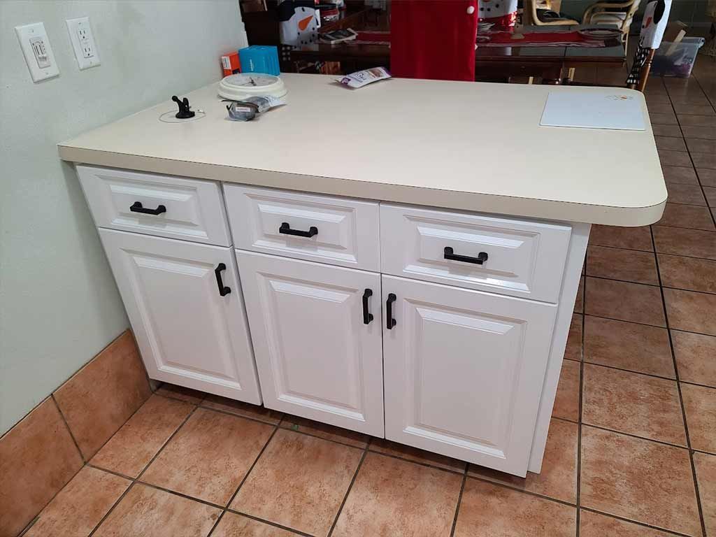 A kitchen island with white cabinets and black drawers.