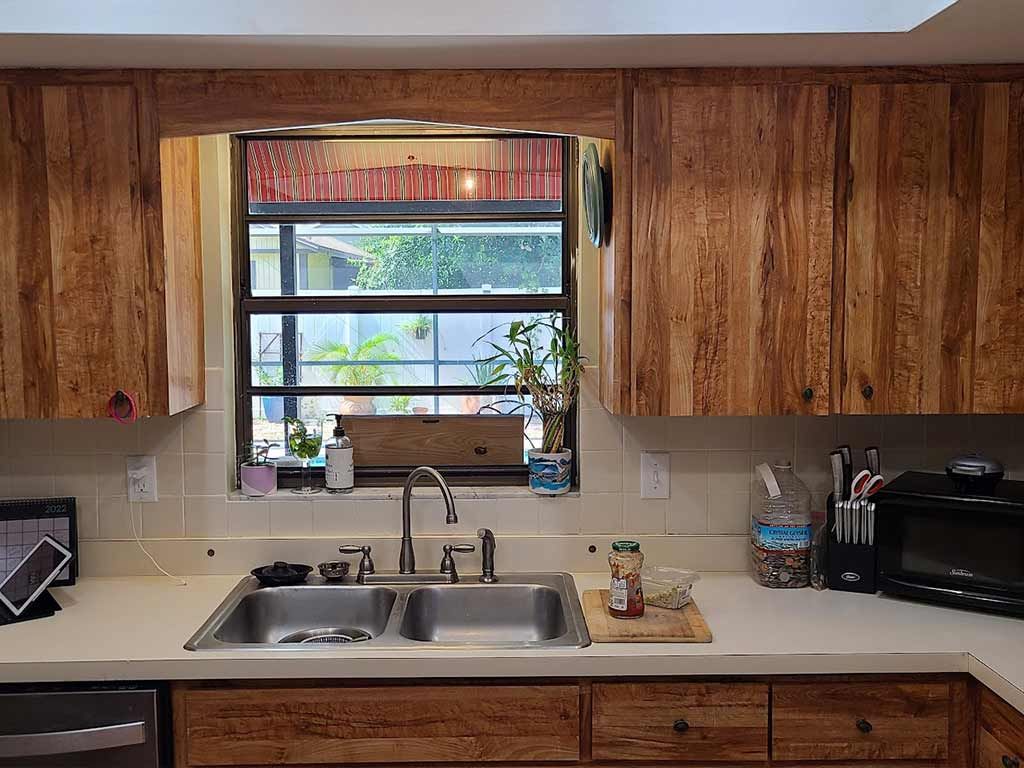 A kitchen with wooden cabinets , a sink , a microwave , and a window.