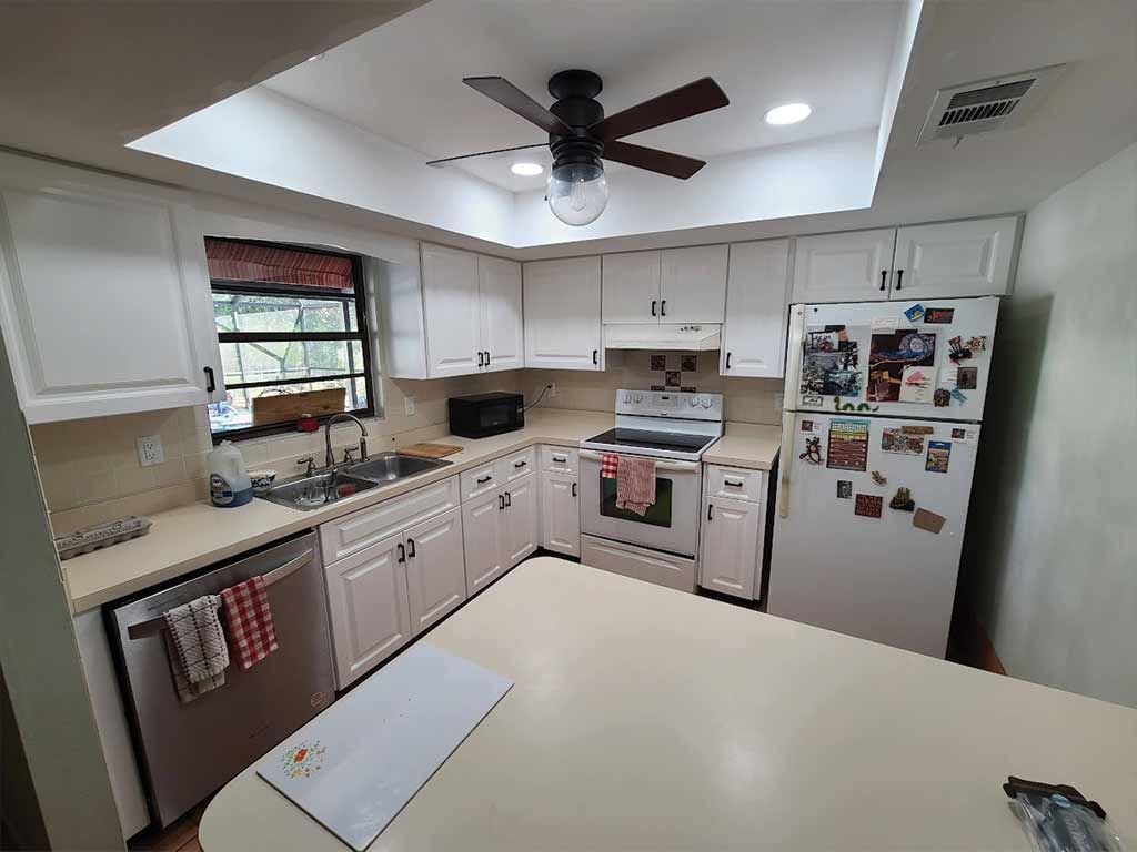 A kitchen with white cabinets , stainless steel appliances , a refrigerator and a ceiling fan.