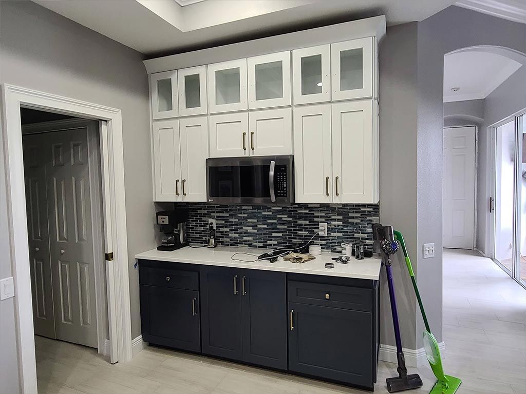 A kitchen with white cabinets , black cabinets , a microwave , and a vacuum cleaner.