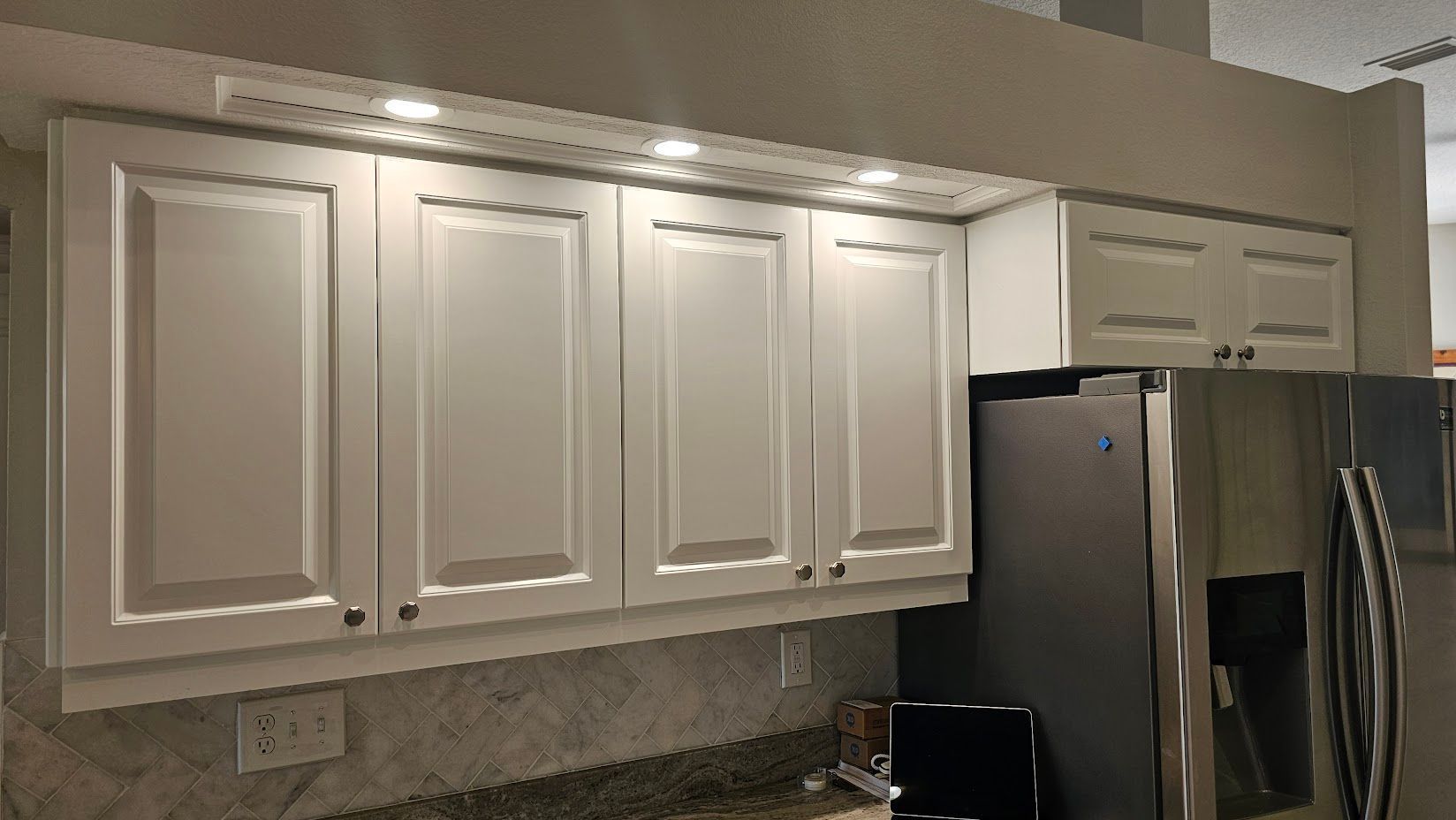A kitchen with white cabinets and a stainless steel refrigerator.