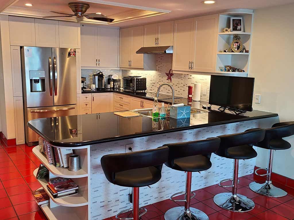 A kitchen with stools, a refrigerator , and a computer on the counter.