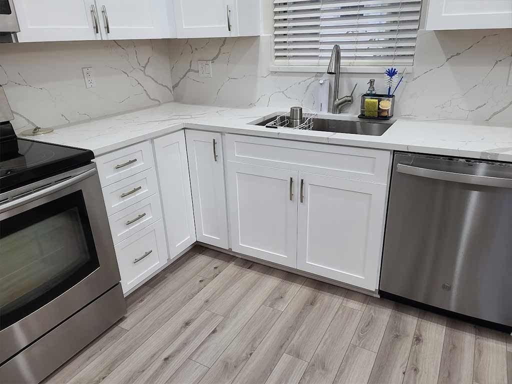 A kitchen with white cabinets , stainless steel appliances , a sink , and a window.