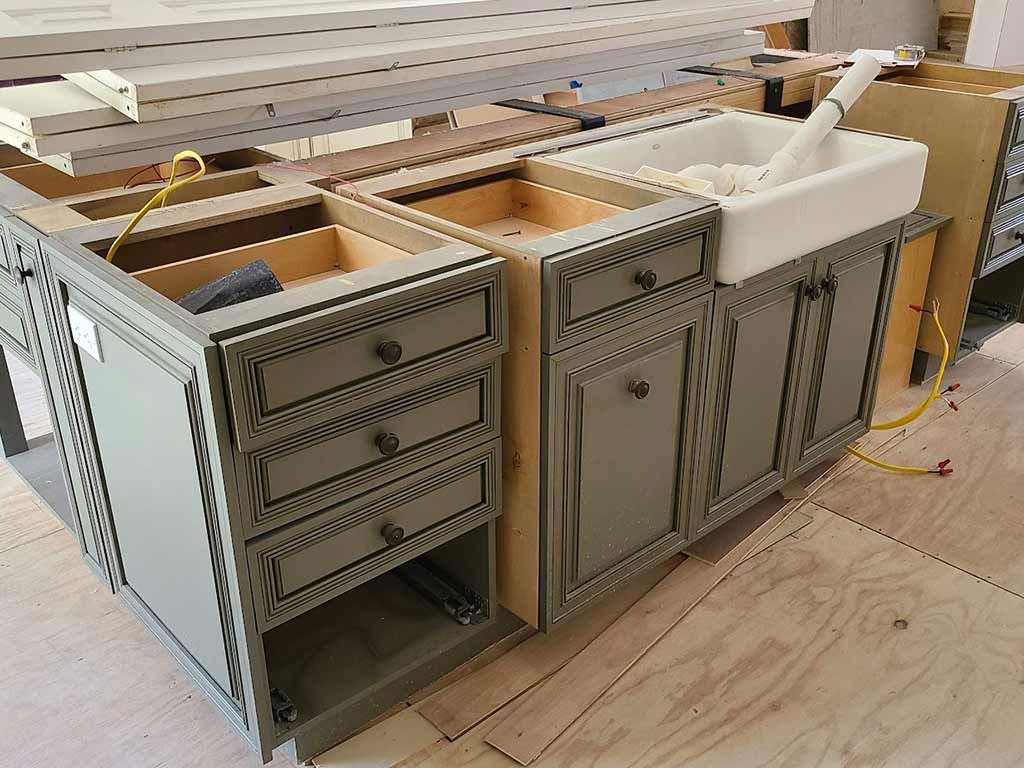 A kitchen is being built with gray cabinets and a white sink.