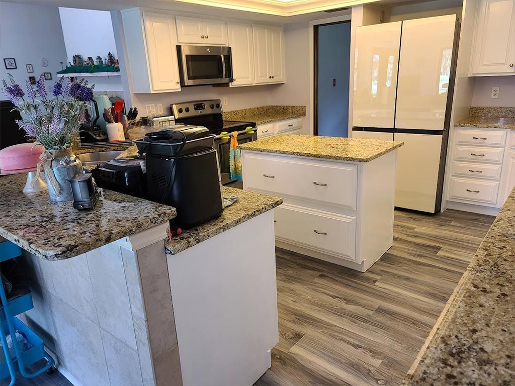 A kitchen with granite counter tops , white cabinets , stainless steel appliances and a large island.