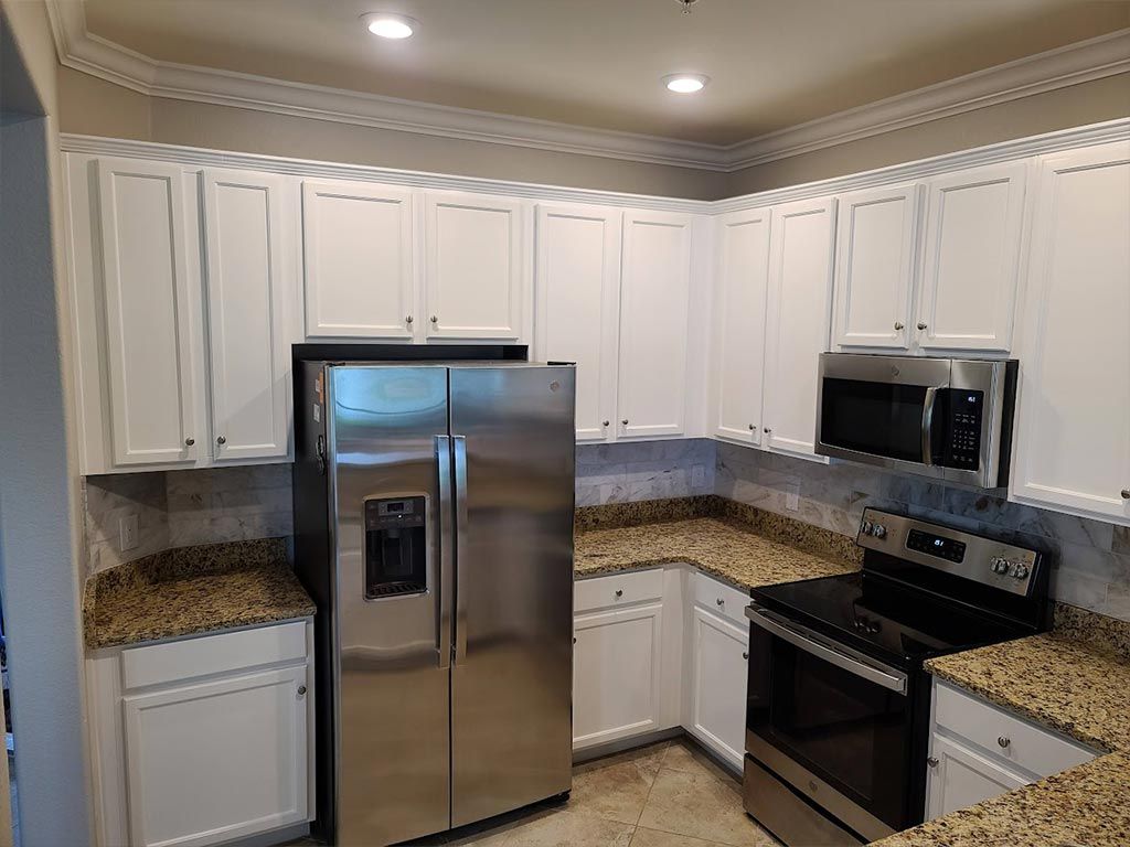 A kitchen with white cabinets , stainless steel appliances , granite counter tops and a refrigerator.