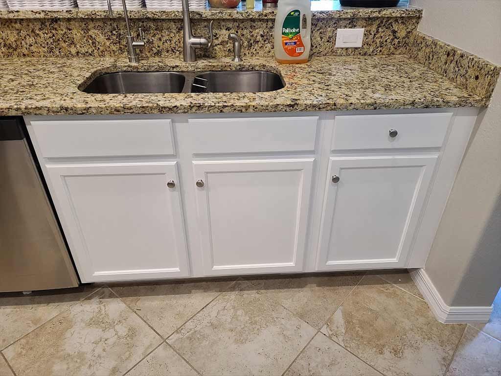 A kitchen with granite counter tops , white cabinets , a sink and a dishwasher.