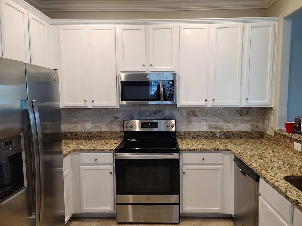 A kitchen with white cabinets , stainless steel appliances , and granite counter tops.