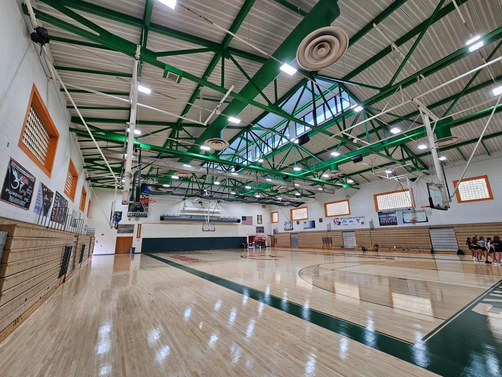 Basketball court with green and wood accents; high ceiling with lighting fixtures.