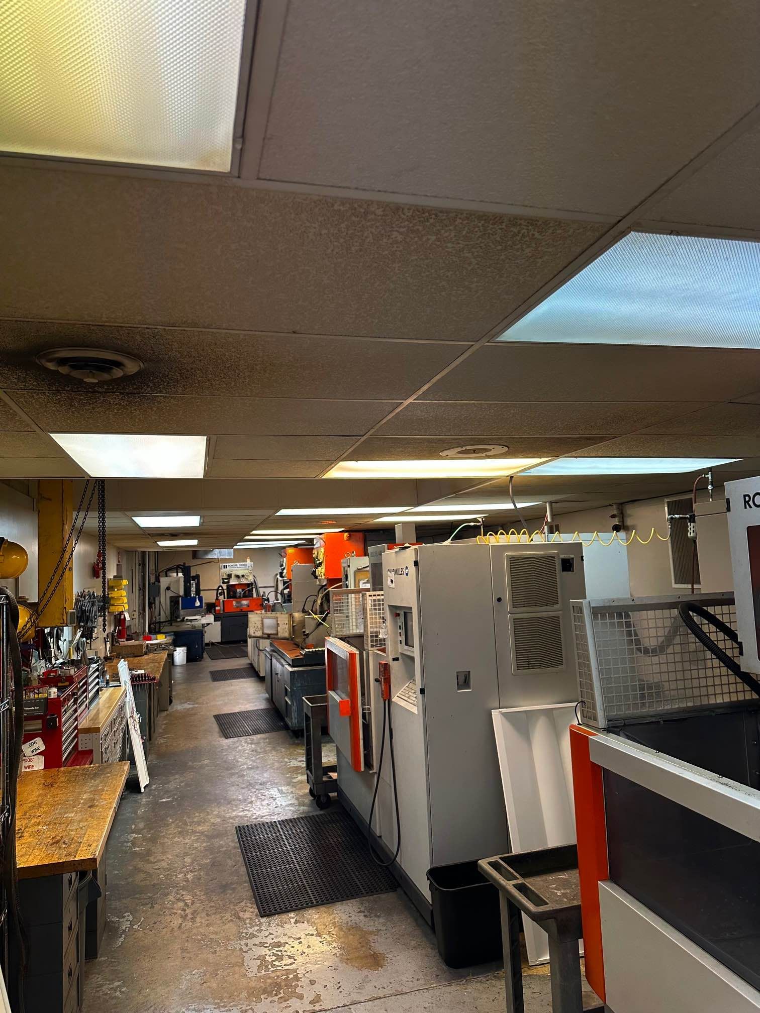 A machine shop interior with several large gray machines, workbenches, and overhead lighting.