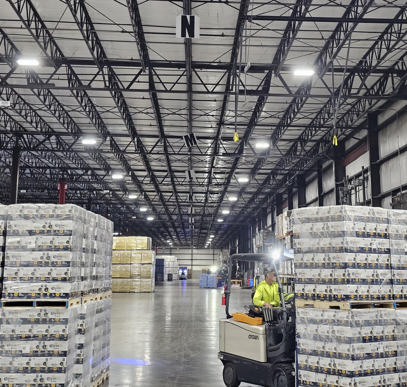 Spacious, high-ceilinged warehouse interior. Several vehicles and construction materials present.