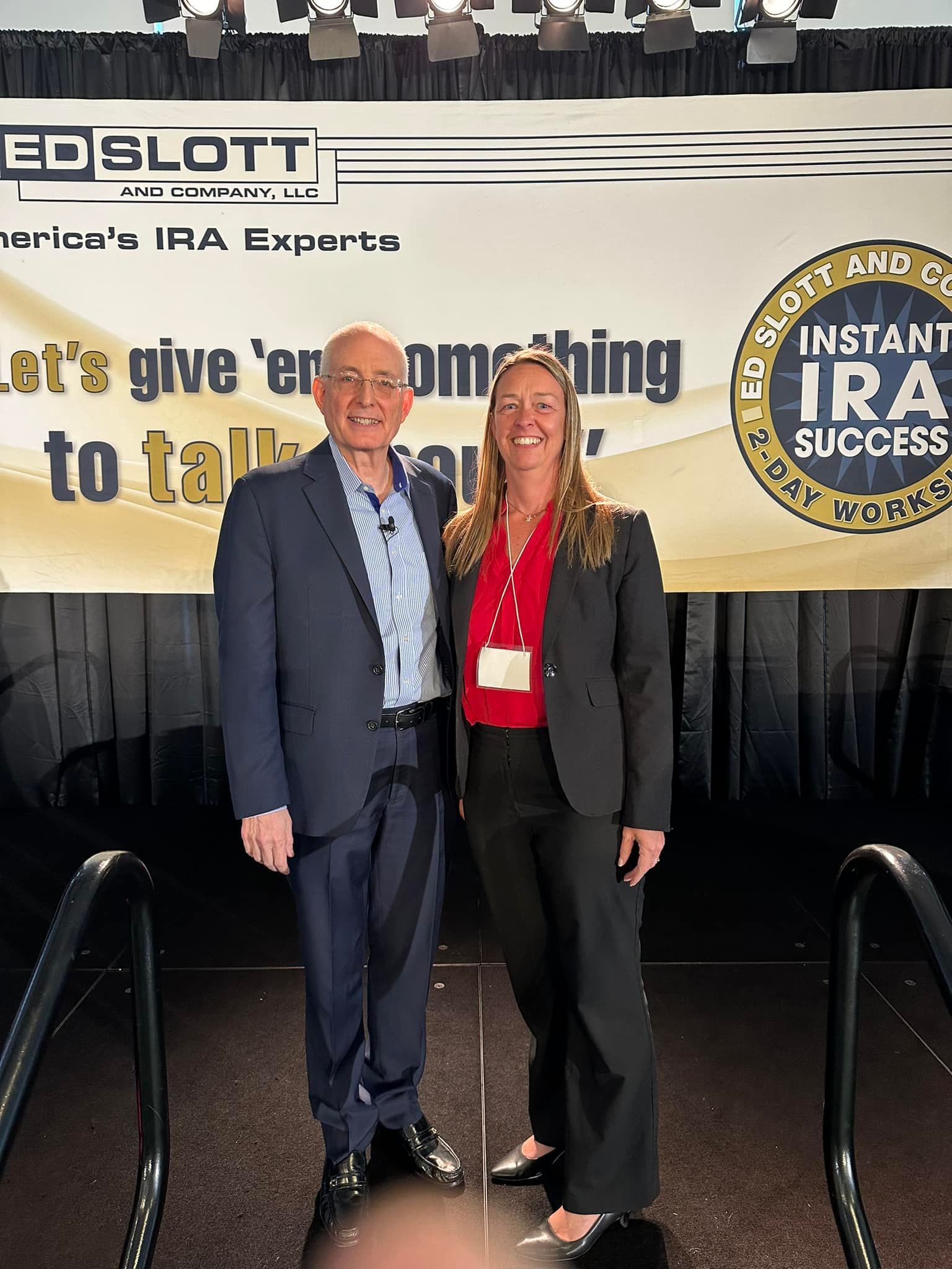 Two people stand on stage in front of a banner. A man and a woman pose with a banner that reads