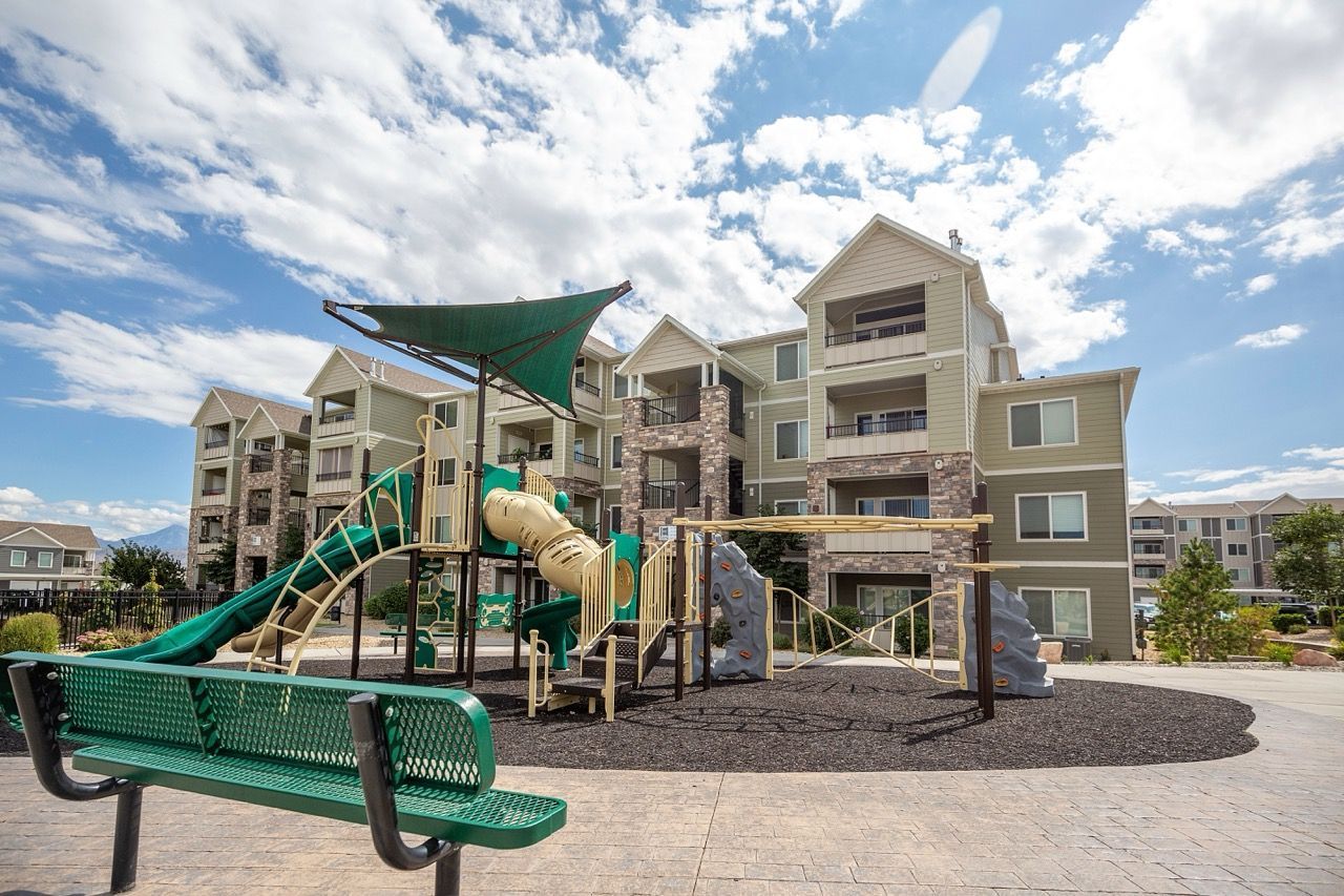 Playground with green slides and climbing structures in front of a multi-story apartment building.