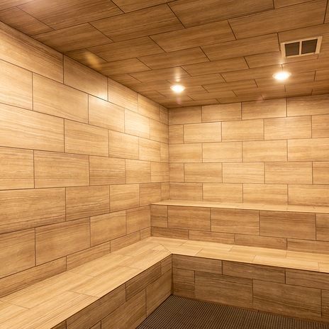 Indoor sauna with wooden tile walls and built-in benches, warm lighting.