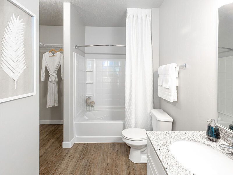 Bright apartment bathroom with a white tub/shower, toilet, and granite vanity.