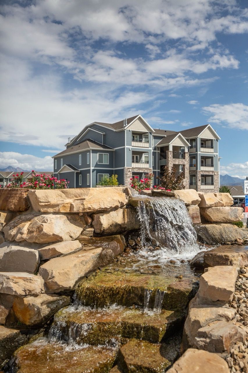 Exterior view of a multi-story apartment building with a stone waterfall feature in front.