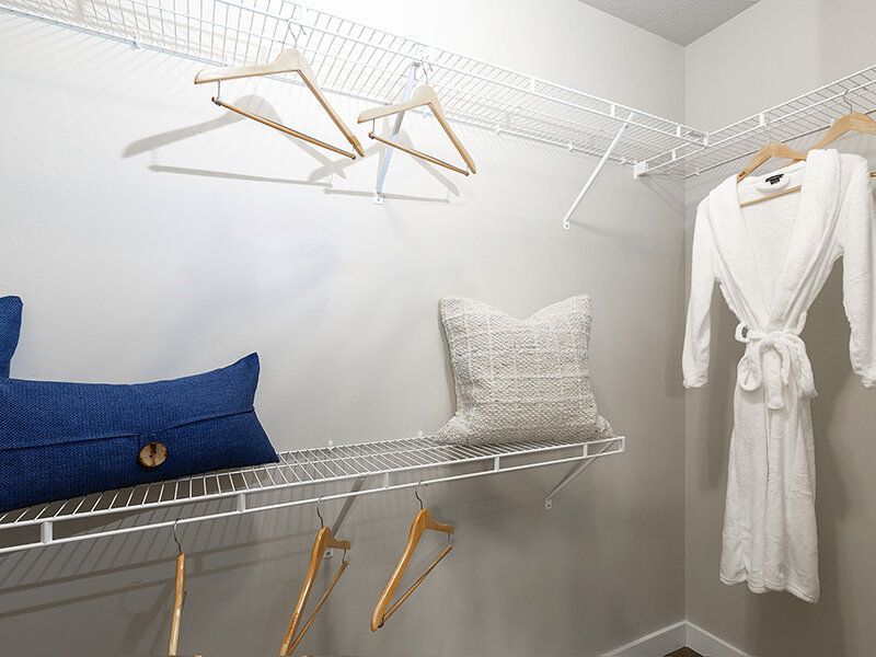 Walk-in closet with white wire shelving, wooden hangers, a robe, and decorative pillows.