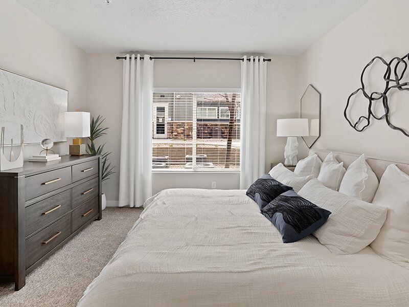 Furnished apartment bedroom with a large bed, white bedding, and a dresser.