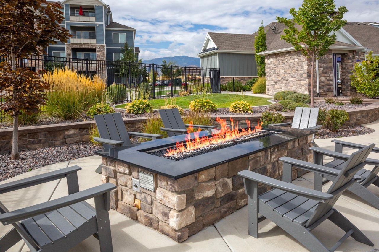 Outdoor communal fire pit with a stone surround and surrounding chairs in a landscaped courtyard.