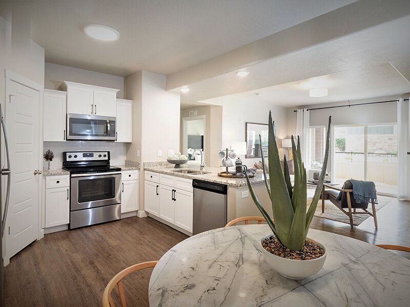 Open-concept kitchen with white cabinets, stainless steel appliances, and a marble dining table.