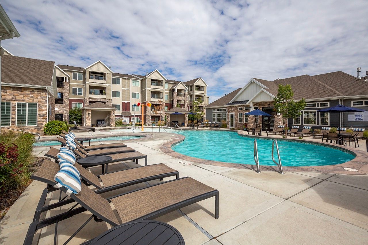 Outdoor pool area at an apartment community with lounge chairs and buildings in the background.