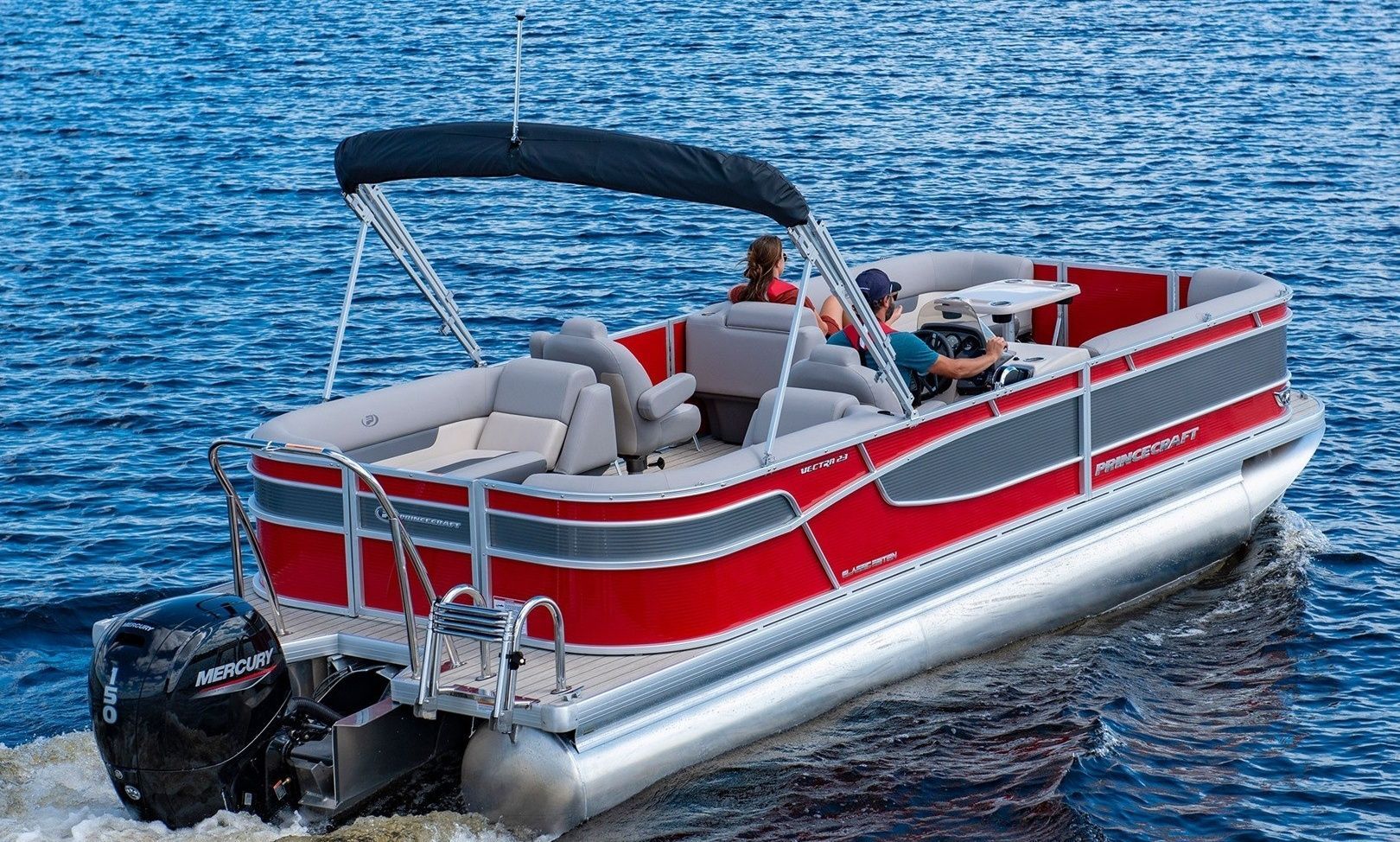 A red and gray pontoon boat is floating on top of a lake.