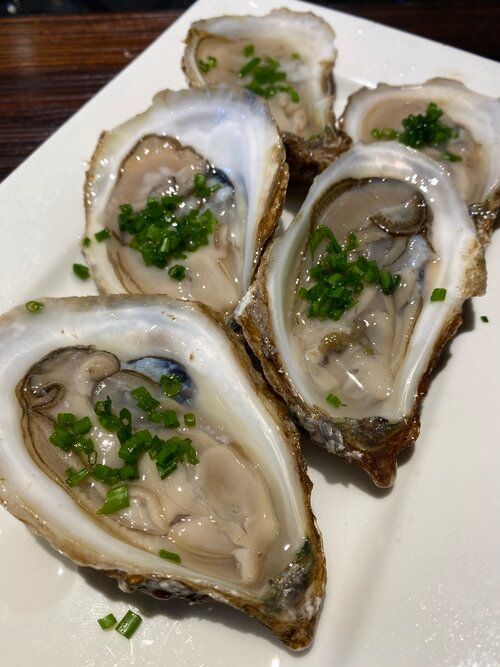 A white plate topped with oysters and green onions