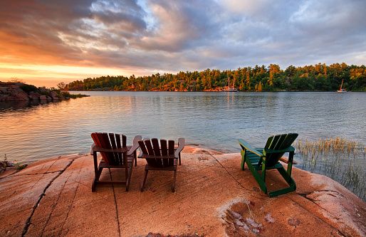 Two chairs are sitting on a rock near a lake at sunset.
