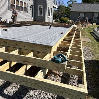 Deck under construction; worker in the background. Wooden frame and gray decking material are visible.