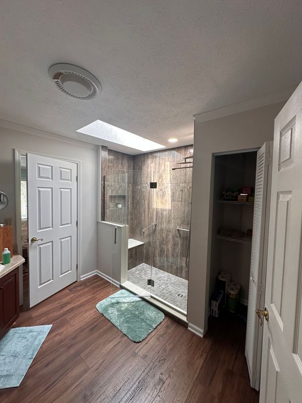 Modern bathroom with a glass shower, wooden vanity, and large mirror. White and gray tones.
