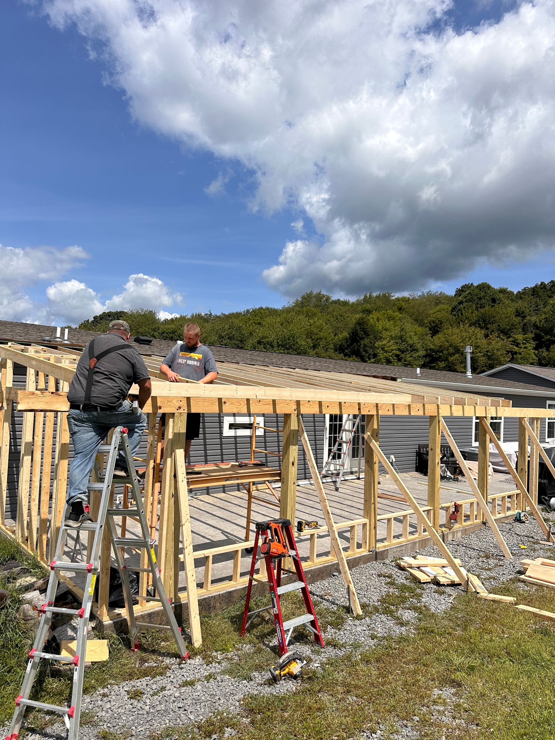 Gray house with workers in front; two gable dormers, windows, front door, and blue sky.