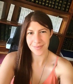 Mujer con cabello largo y castaño con una camiseta sin mangas naranja sonriendo frente a estanterías.