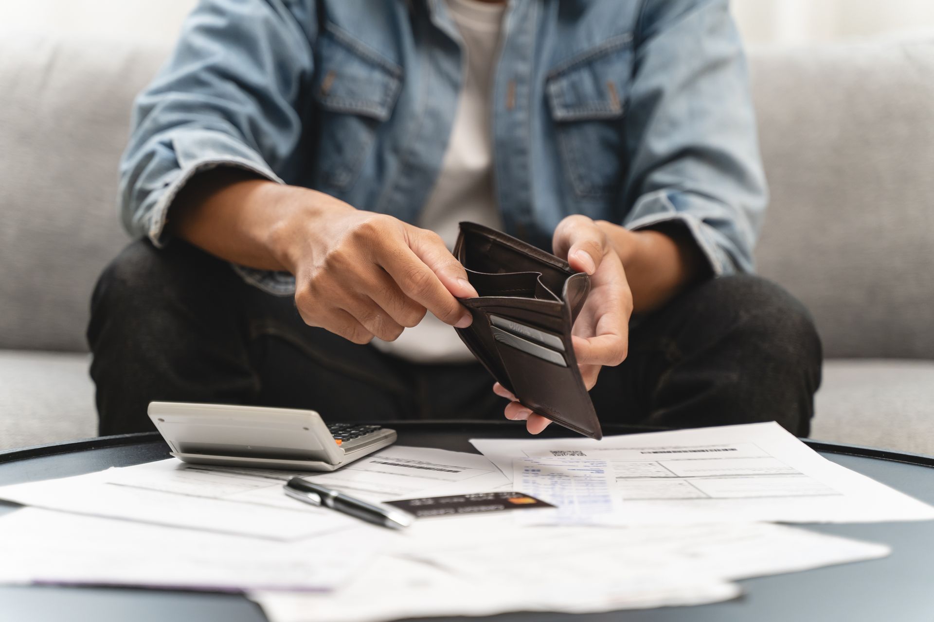 Person with empty wallet, bills, and calculator, looking financially distressed. Person with empty wallet, bills, and calculator, looking financially distressed.