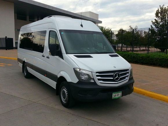 Una furgoneta Mercedes blanca está estacionada frente a un edificio.