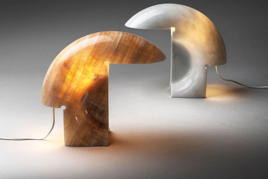 Due lampade da tavolo curve e luminose, una ambrata e una argentata, su una superficie bianca.
